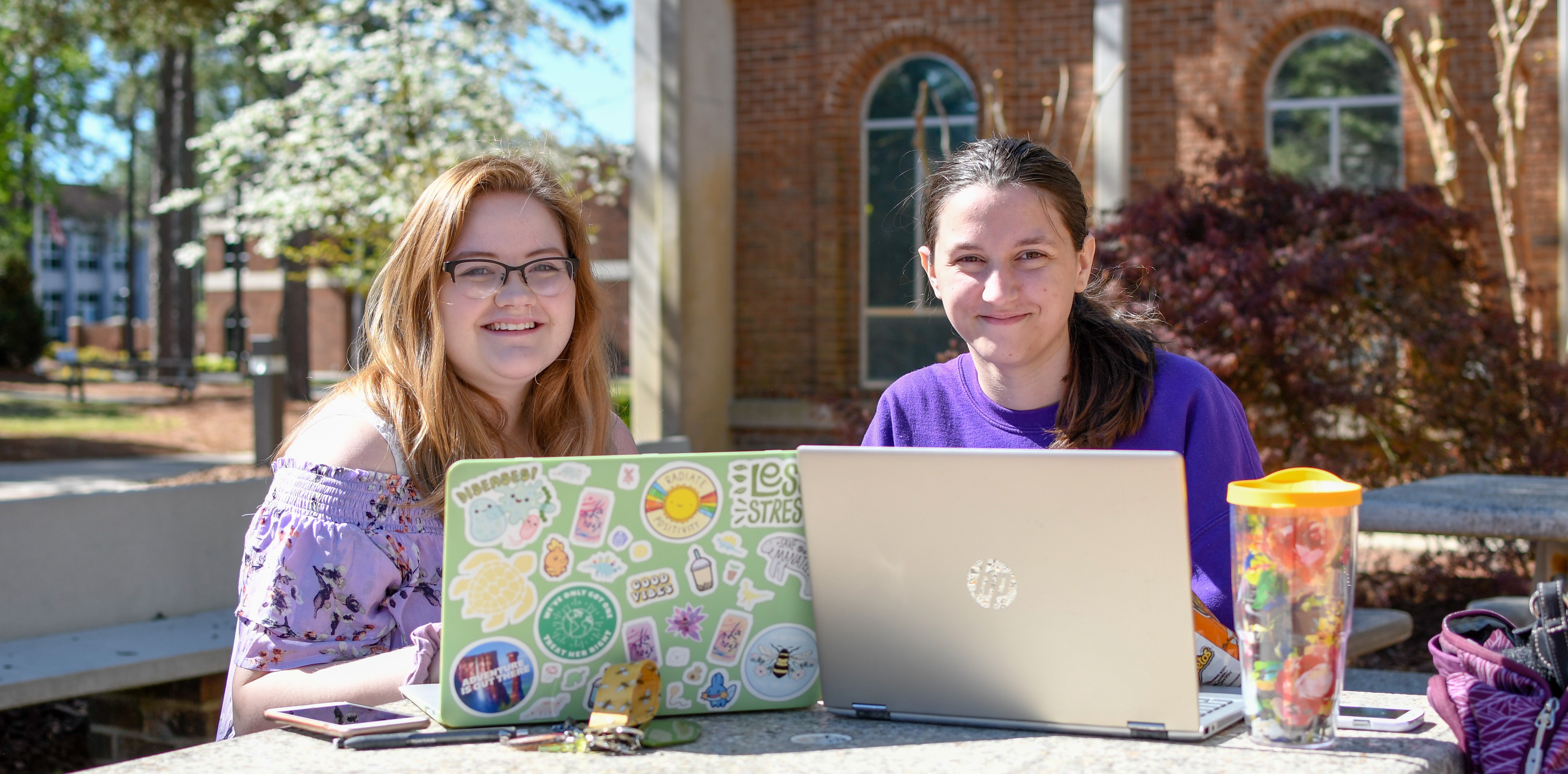 two students outside using laptops